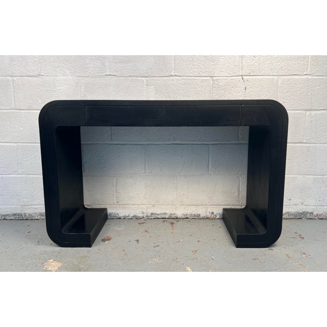 A mid-century modern console table wrapped in sleek black vinyl for a bold, streamlined look. The piece includes a...