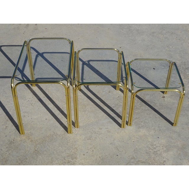 Set of 3 nesting tables in gold-tone metal and glass. Gold-tone metal frame in a tubular shape. 5 mm thick tempered glass...