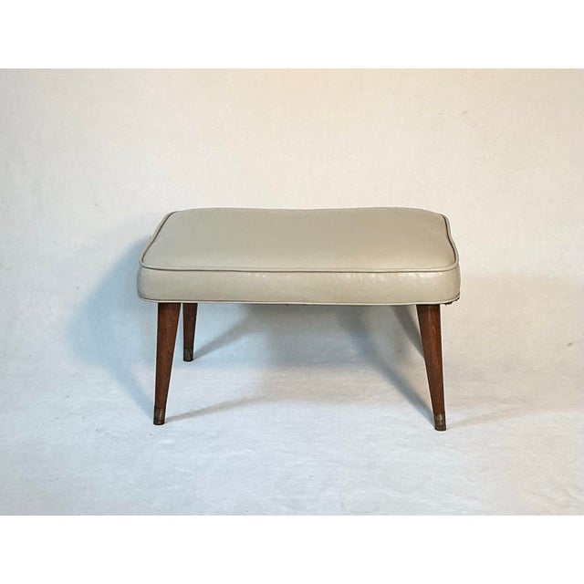 Vintage Mid Century Modern footstool in white vinyl with walnut wood tapered legs with brass feet. All original from the...