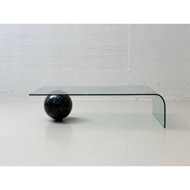 Sculptural coffee table by italian designer giorgio cattelan, featuring a curved glass top that appears to rest...