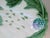 A plate that can be used for asparagus or artichokes. It has raised green leaves and purple tips against a cream...