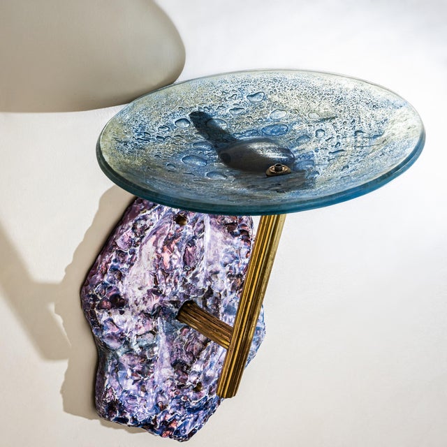 Wall-mounted bowl sconce in blue glass with characteristic air bubble inclusions and a ribbed brass mount. The wall...
