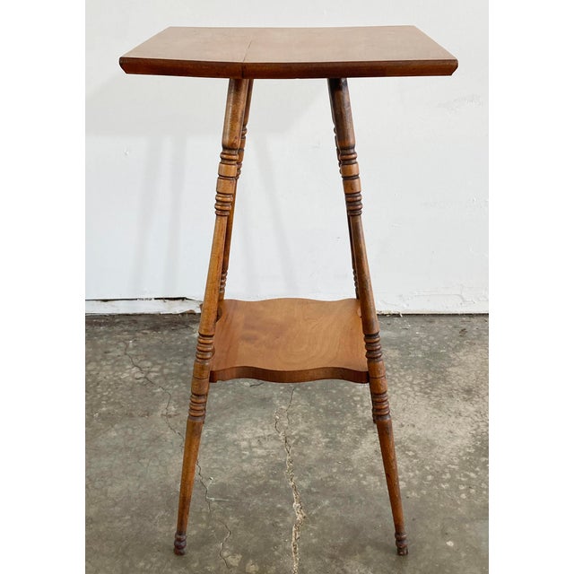Handmade antique two tier side table with four petite turned splay wood legs attached by lower stretcher shelf. Square top...
