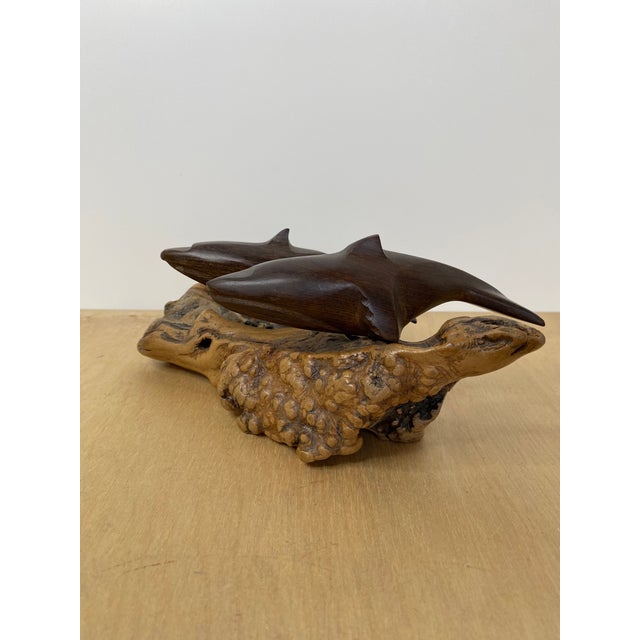 Hand carved Two dark brown wooden dolphins in a leaping pose, mounted on a piece of driftwood with a natural brown finish....