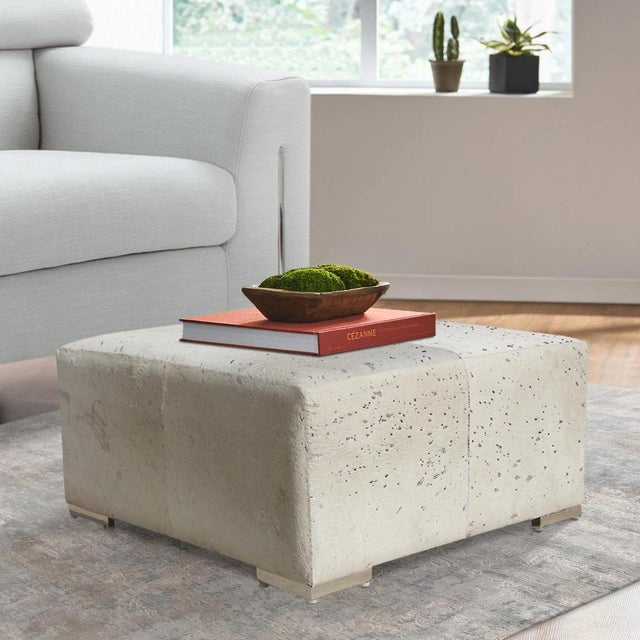 A bold and luxurious statement piece, this large square ottoman is upholstered in natural cowhideenhanced with elegant...