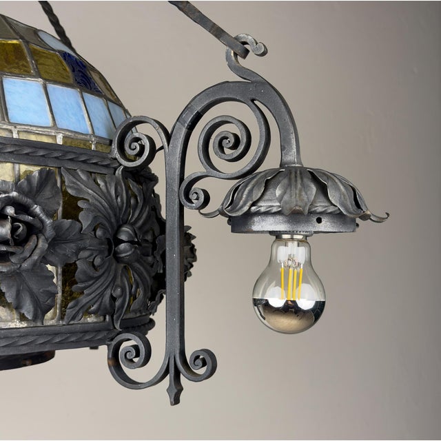 Italian vintage wrought iron chandelier featuring floral metalwork, decorative scrolls, and a colorful stained glass...