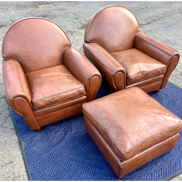 A pair of exquisite French Art Deco Saddle Leather chairs and ottoman from the 20th century. These sumptuous club chairs...