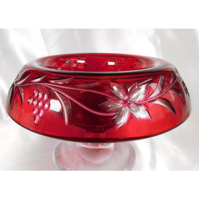This is a red cut to clear compote with a clear base. The compote is cut in a grape and leaf design on the folded over...