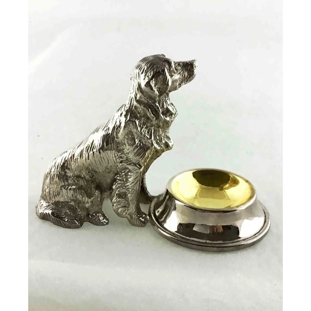 A metal silver plated a Dog, I think the Breed is a Retriever sitting next to an attached bowl that is used as an open...