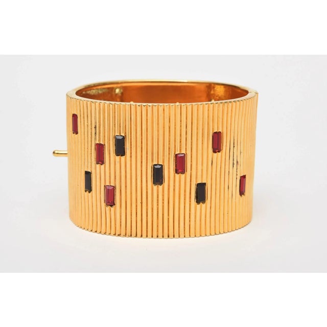 This is part of Chairish’s Costume Jewelry assortment. This wide-ribbed cuff gold toned Bracelet, with red and black glass...