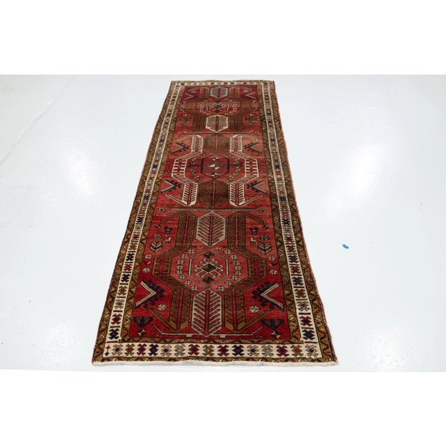 Vintage Persian Heriz runner. This wool rug has a rust-red color field with brown, blue, and beige accents all over the...