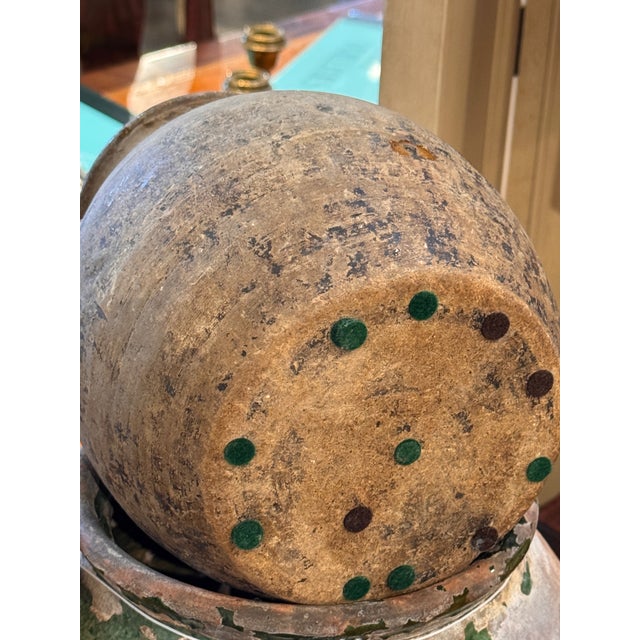 A small terracotta jug with a rounded body, short neck, and opposing loop handles. The surface shows a naturally worn...