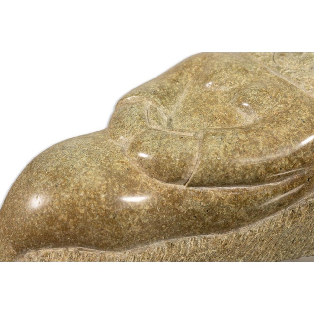 A sculpted Inuit figure, this hand-carved soapstone sculpture depicts a resting man in traditional garb, his body gently...