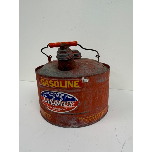 Galvanized metal gasoline can with distressed red painted finish, applied graphics, and wood handle. Styled after early...