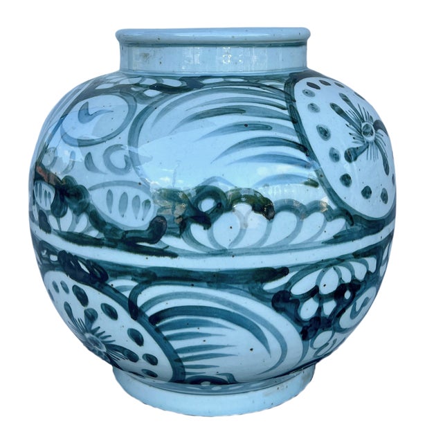 Bold and sculptural, this hand-painted blue and white jar features a stylized sunflower motif framed by sweeping...