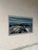 This panoramic landscape painting captures a sweeping coastal view with rocky shores under a dramatic sky. The expressive...
