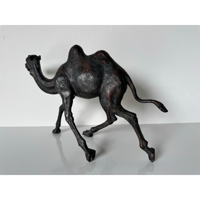 A striking vintage cast bronze sculpture of a camel in mid-stride, exuding movement and elegance. This intricately...