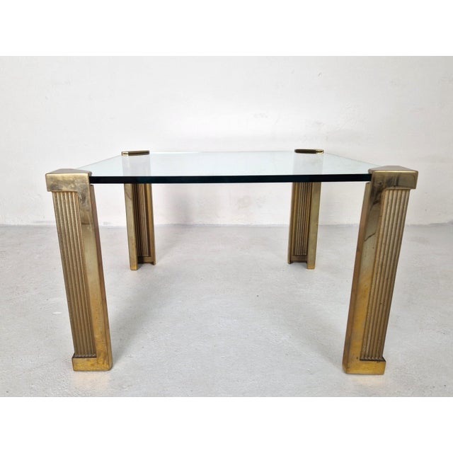 Iconic design by Hungarian designer Peter Ghyczy from the 1970s. This side table has thick brass legs and a thick glass...