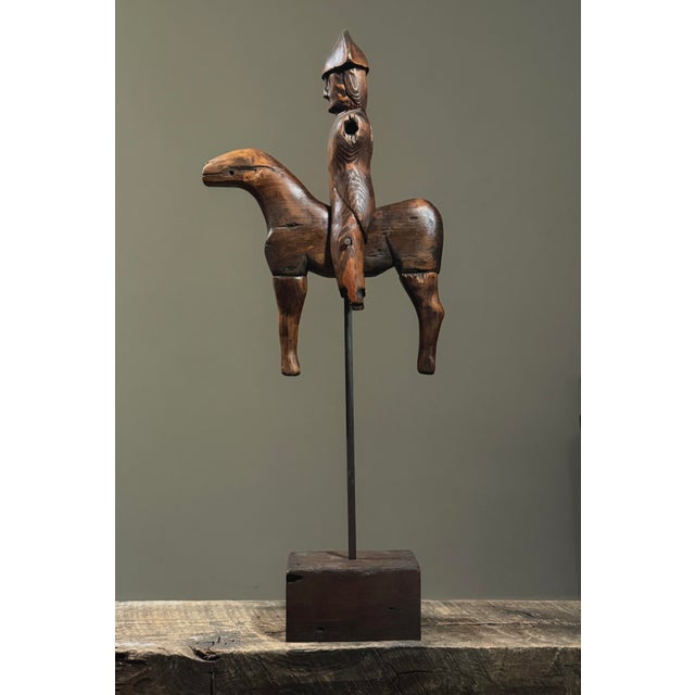 A vintage hand carved folk art sculpture depicting a soldier seated atop a horse, mounted on a rod and stained wooden...