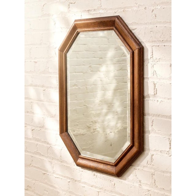 A handsome vintage wall mirror featuring an angular octagonal silhouette framed in warm walnut-toned wood. The beveled...