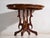 This antique salon table in walnut wood presents an oval top with a shaped outline over a four-armed central pedestal....