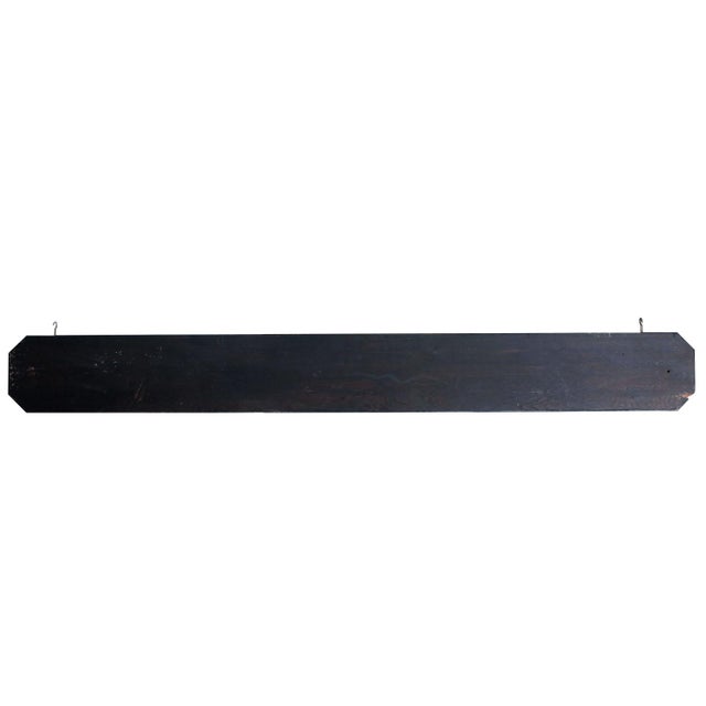A painted black & gold wooden sign, "The Armoire" with hooks that are 66" apart.
