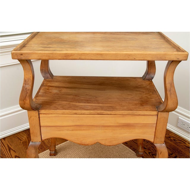 An antique French Provincial two-tier side or end table in a warm honey-toned fruitwood with a galleried top, lower shelf,...
