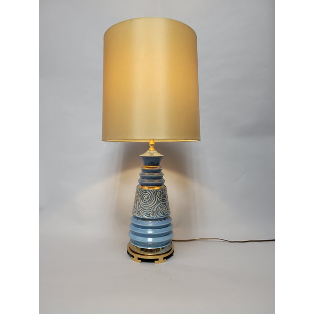 Mid-Century Lamp in a light blue glaze with a scrolling carved design and metallic gold accents. The brass base is a later...