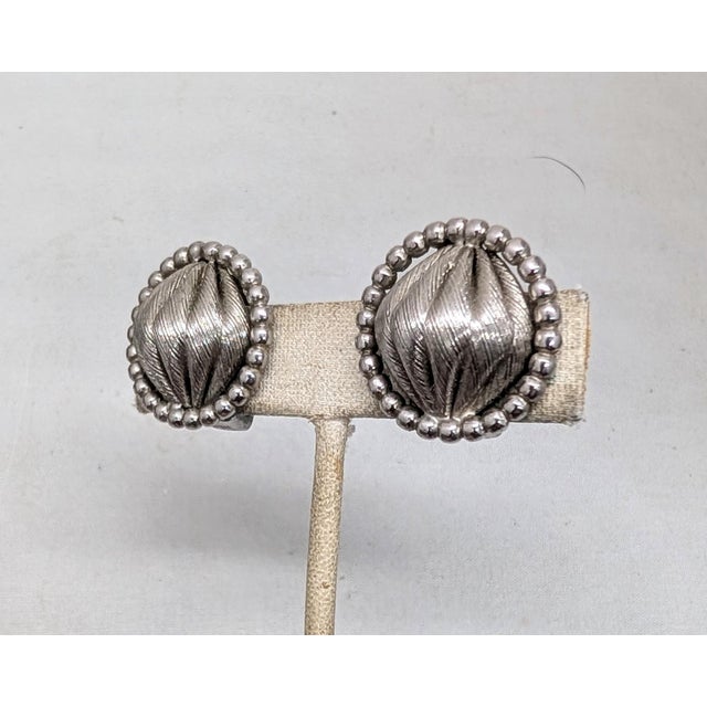 Circa 1961 round rhodium plated "gathered" center with round nubs around the edges clip earrings. Marked "NAPIER PAT....