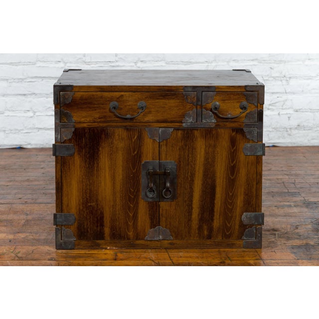 An antique Korean brown wood side cabinet from the 19th century with iron hardware, drawers, and doors. Created in Korea...