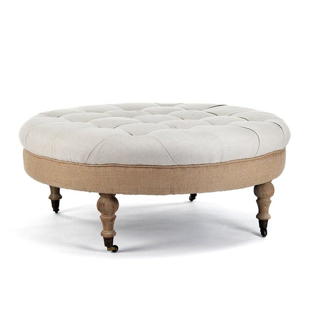 The Maison Tufted Round Ottoman from Zentique features a generous round button-tufted top on turned wood legs with brass...