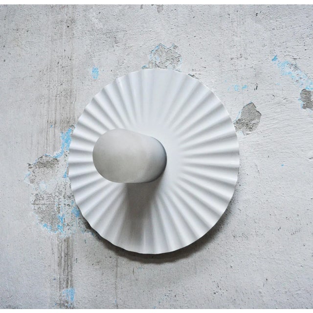 This ceiling or wall lamp features a disc-shaped reflector in sheet metal with a radial pleating. In the centre, screwed...