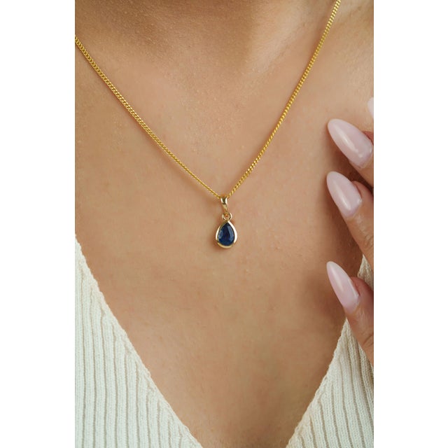 This solitaire pendant showcases a 0.7 carat natural pear-cut blue sapphire, set in 14K yellow gold. The sapphire...