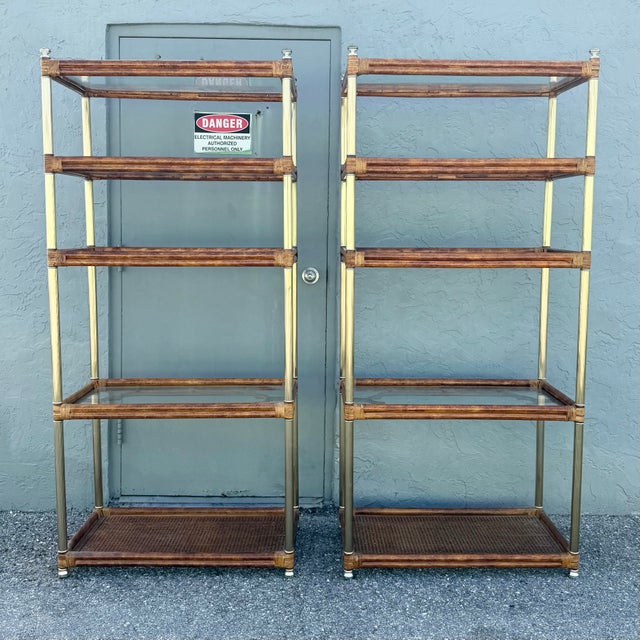 A striking pair of vintage Palm Beach Chic étagères featuring warm rattan frames accented with slender fluted gold-tone...