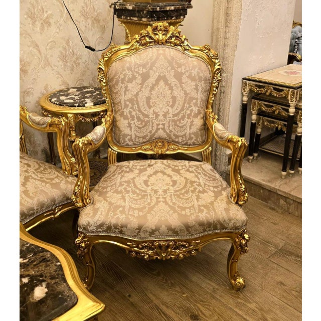 A stunning French Rococo-style armchair featuring luxurious beige damask upholstery and an elaborately carved wooden frame...
