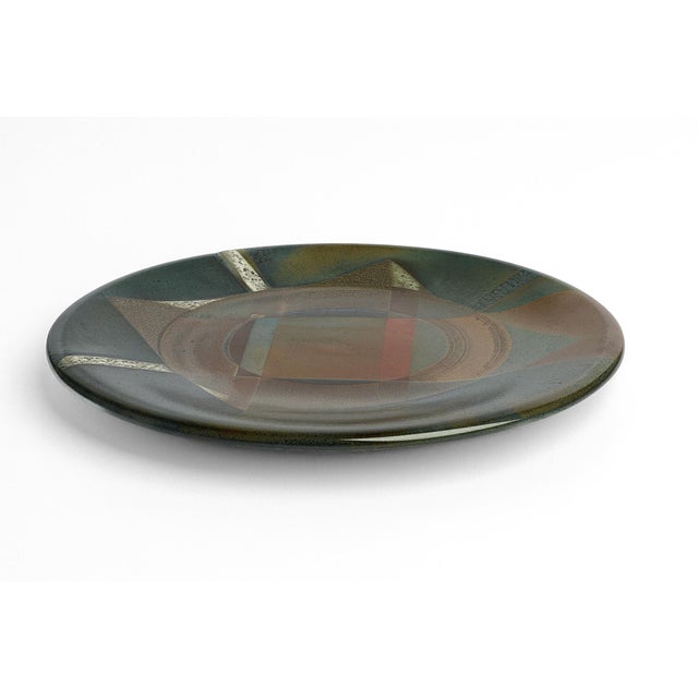 A large studio plate finished in rusted colors of blue and green. Its wide diameter and shifts in color create a subtle,...