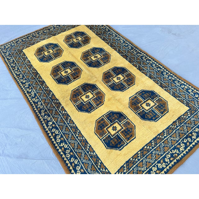 This hand-knotted Ersari rug showcases a row of bold octagonal "gul" medallions in deep navy and brown, set against a warm...