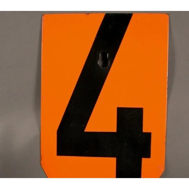 This flat metal sign number is enameled and stenciled.