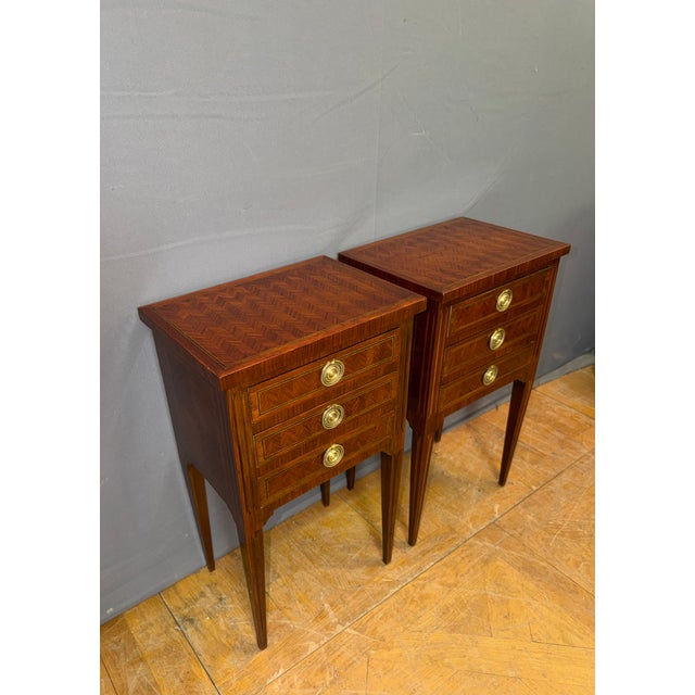 A pair of Louis XVI style bedside tables in mahogany marquetry with native wood stringing. They each have three drawers in...