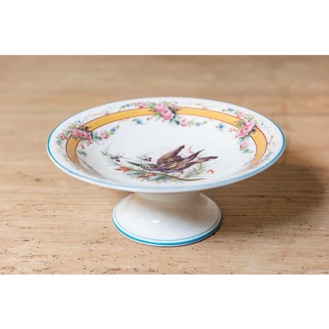 A beautifully hand-painted porcelain compote dish featuring an elegant pedestal form and richly detailed decoration. The...