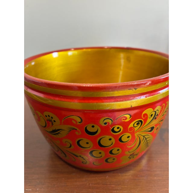 Vintage hand-painted wooden bowl featuring bold red coloring with ornate gold and black folk art floral detailing. The...