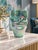Sculptural art glass vase featuring an aqua-green body, flowing darker swirls, and a luminous iridescent finish. Depending...