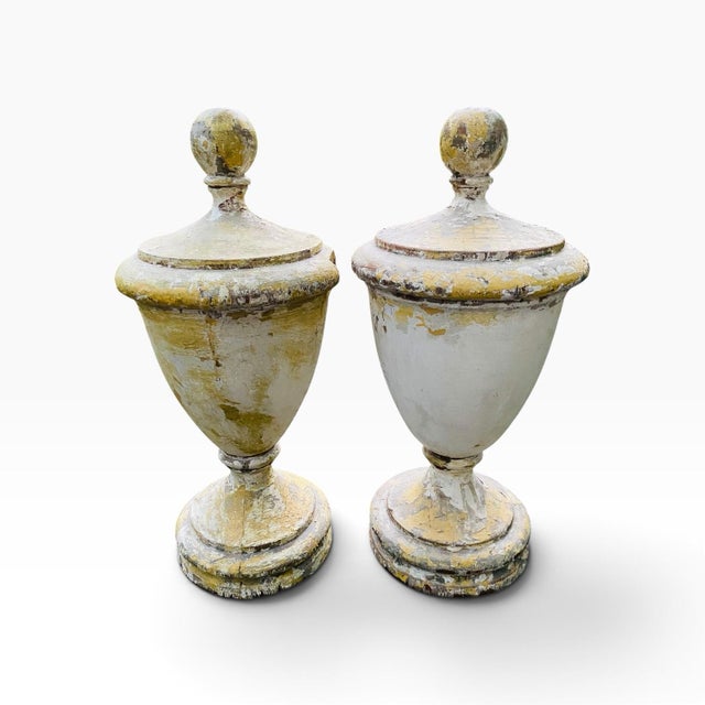 A pair of matching carved wood finials with layers of perfectly worn paint and a weathered patina. One finial has a loss...