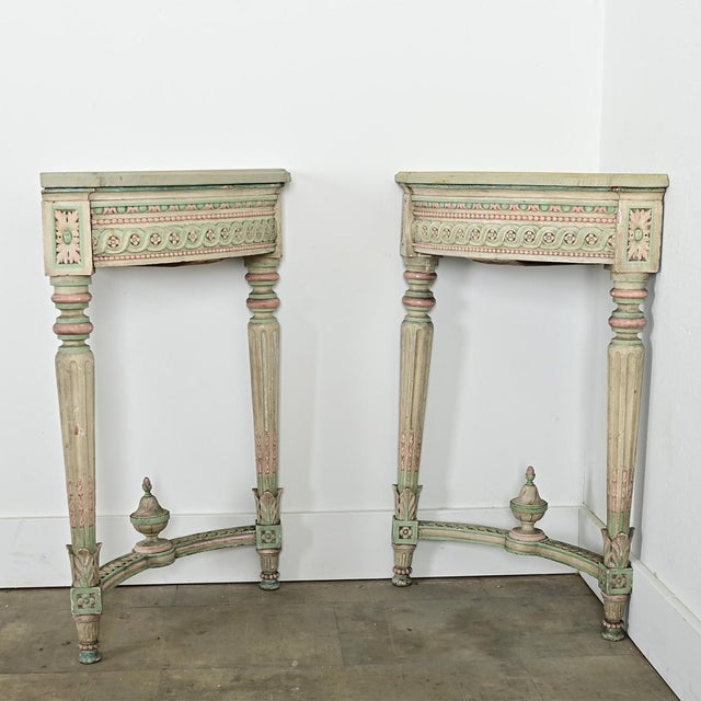 A matching pair of elaborately carved and painted vintage French quarter-round corner tables that are Louis XVI in style...