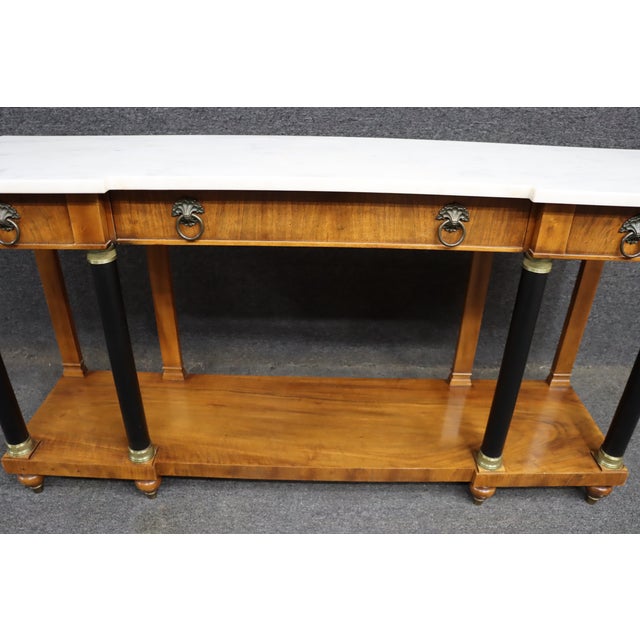 Refined neoclassical console table by John Widdicomb, featuring a white marble top with shaped ends over a warm-toned wood...