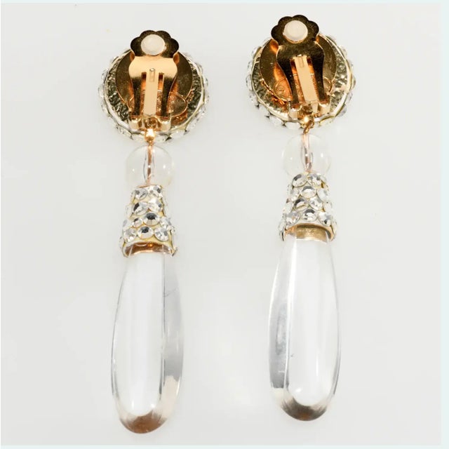 Dangle earrings adorned with clear flat backed rhinestones and large Lucite teardrops. Marked James Arpad although you...
