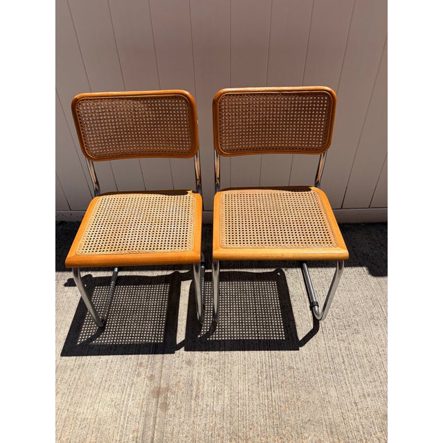 Stylish pair of vintage cantilever dining chairs featuring tubular chrome frames, warm wood trim, and woven cane seats and...
