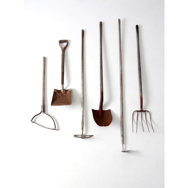 A charming collection of six early 20th century garden tools featuring weathered wood handles and aged iron heads. The...