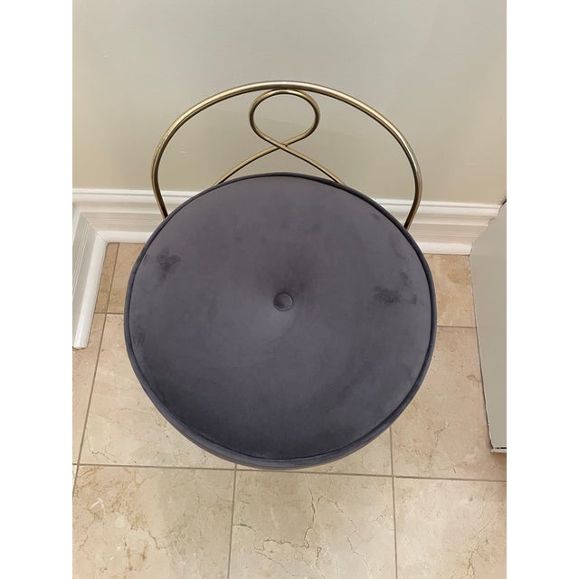 Vintage Hollywood Regency–style vanity stool featuring a sculptural gold-tone metal frame paired with a plush gray velvet...