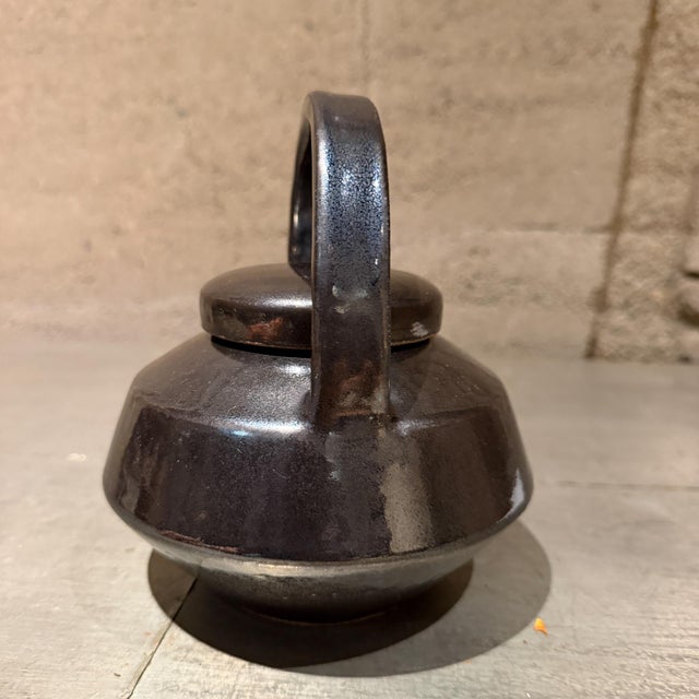 For your consideration, a dark, glossy glazed ceramic teapot featuring a rounded body, a prominent overhead arched handle,...
